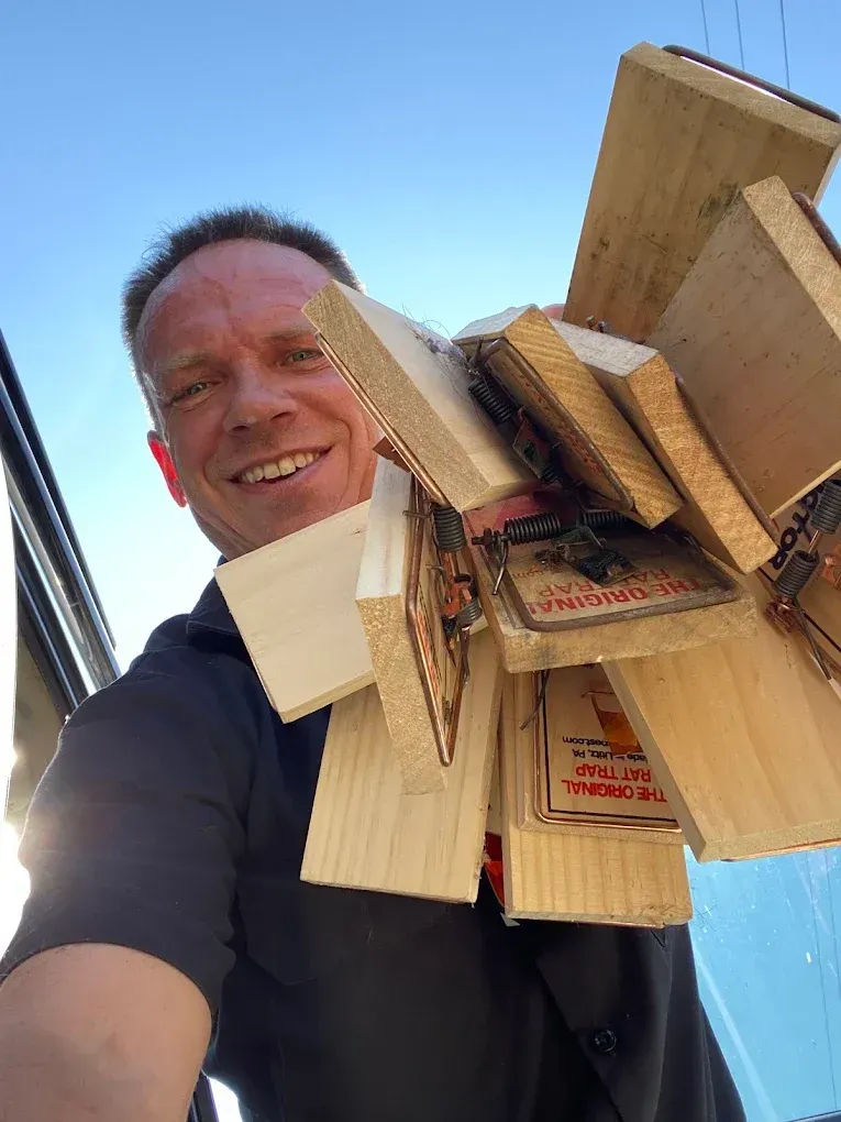 Man smiling and holding a large stack of wooden boards outdoors against a blue sky