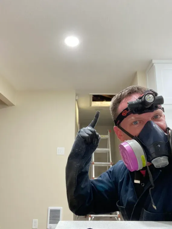 Person wearing a respirator and headlamp points at an open wall vent in a room under renovation