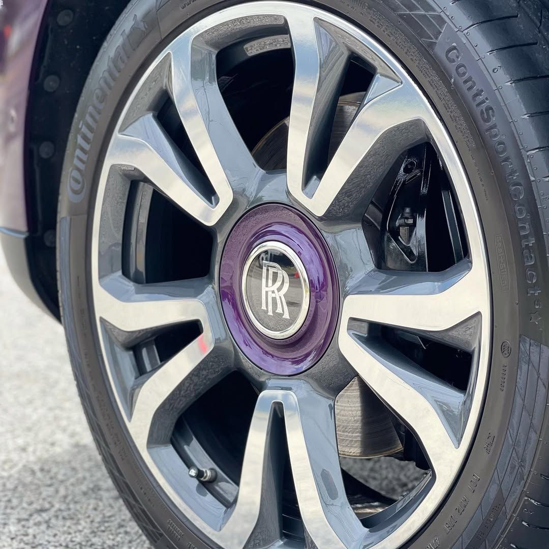 Close-up of a Rolls-Royce wheel featuring a purple center cap with the double R logo on a polished metallic rim.