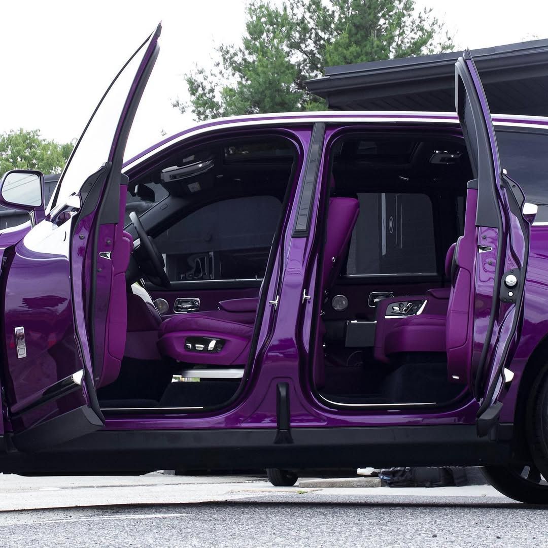 A side view of a purple luxury SUV with its suicide-style doors open, revealing a matching purple leather interior.