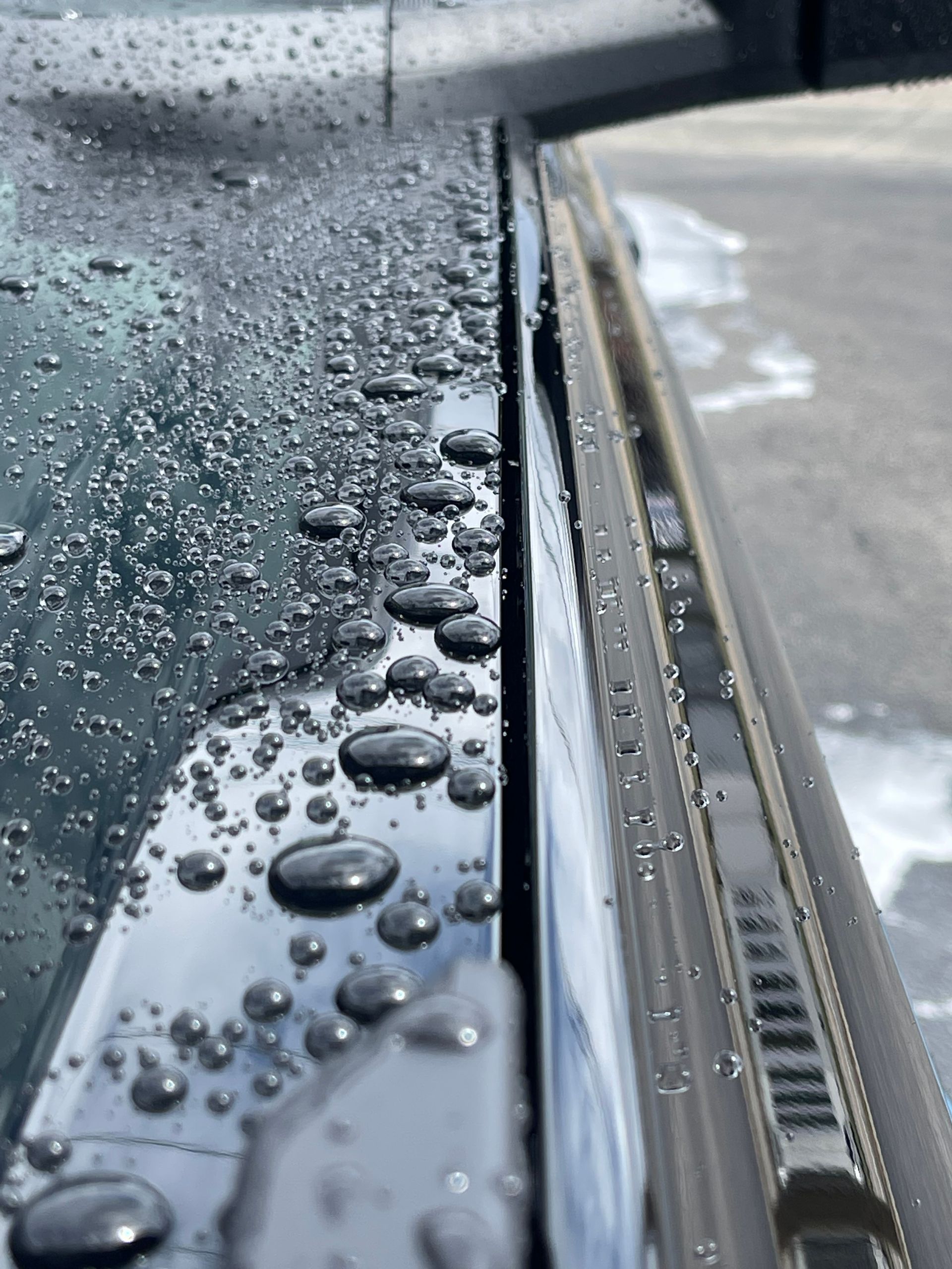 A close-up view of raindrops on a car windshield and the adjacent black frame, showing a gap between the two surfaces.