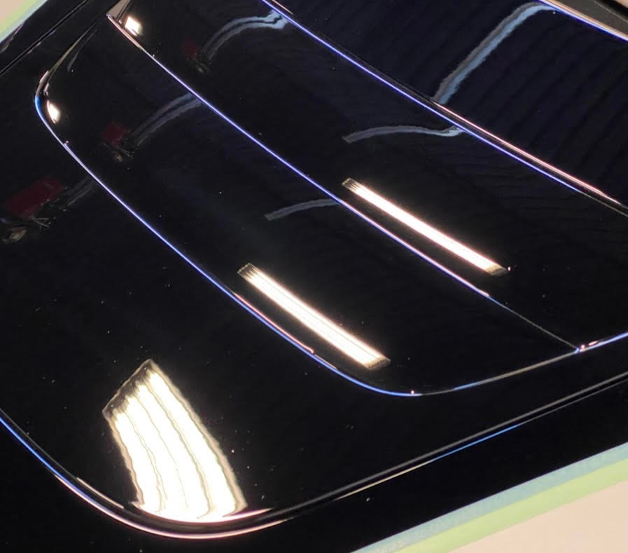 Bright blue car door with masking tape on the handle, showing a reflection of shop lights.