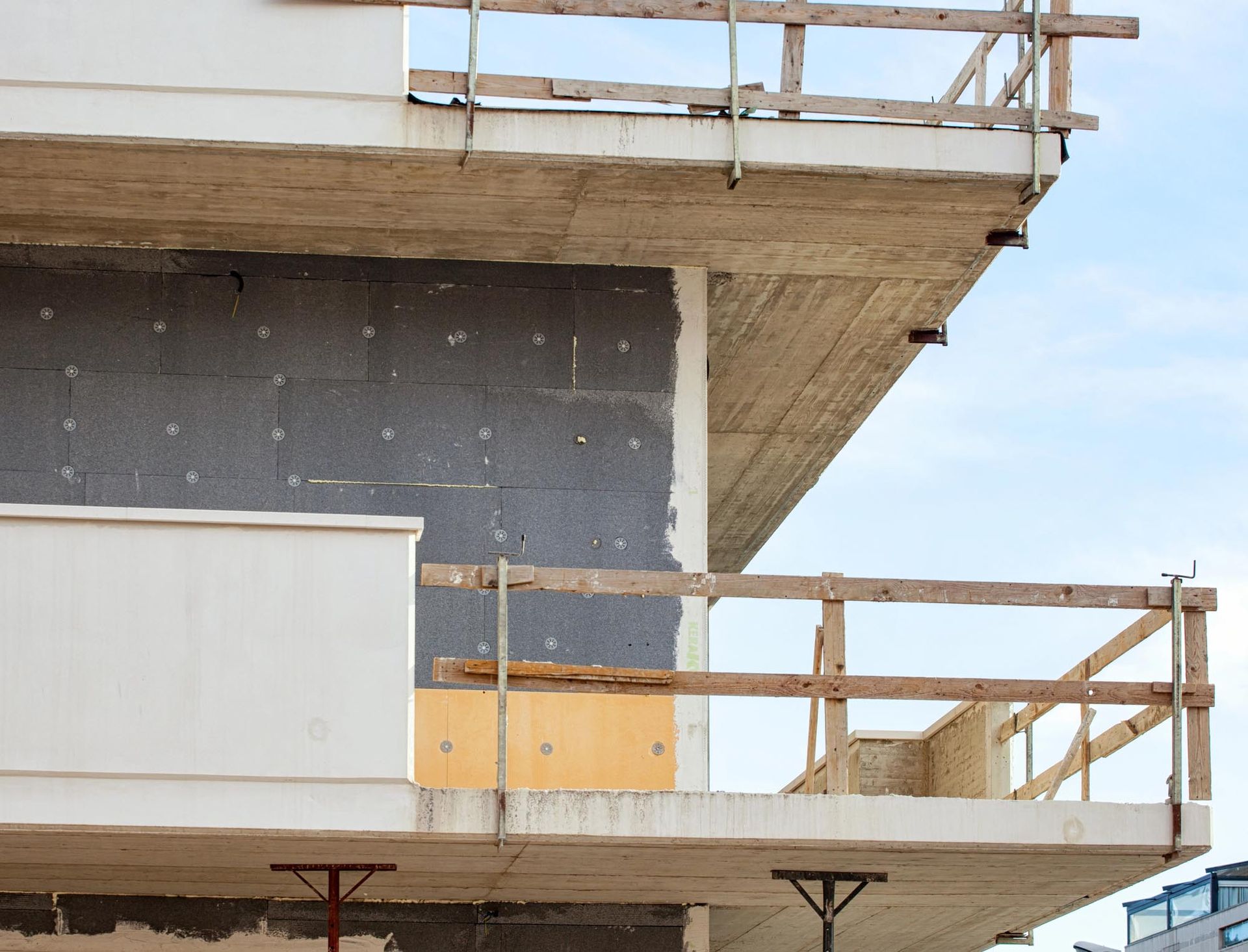 Due balconi sovrapposti su un edificio moderno in costruzione, ancora in fase di completamento, con pannelli isolanti grigi e gialli a vista.