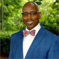 A man in a blue suit and bow tie is smiling for the camera.