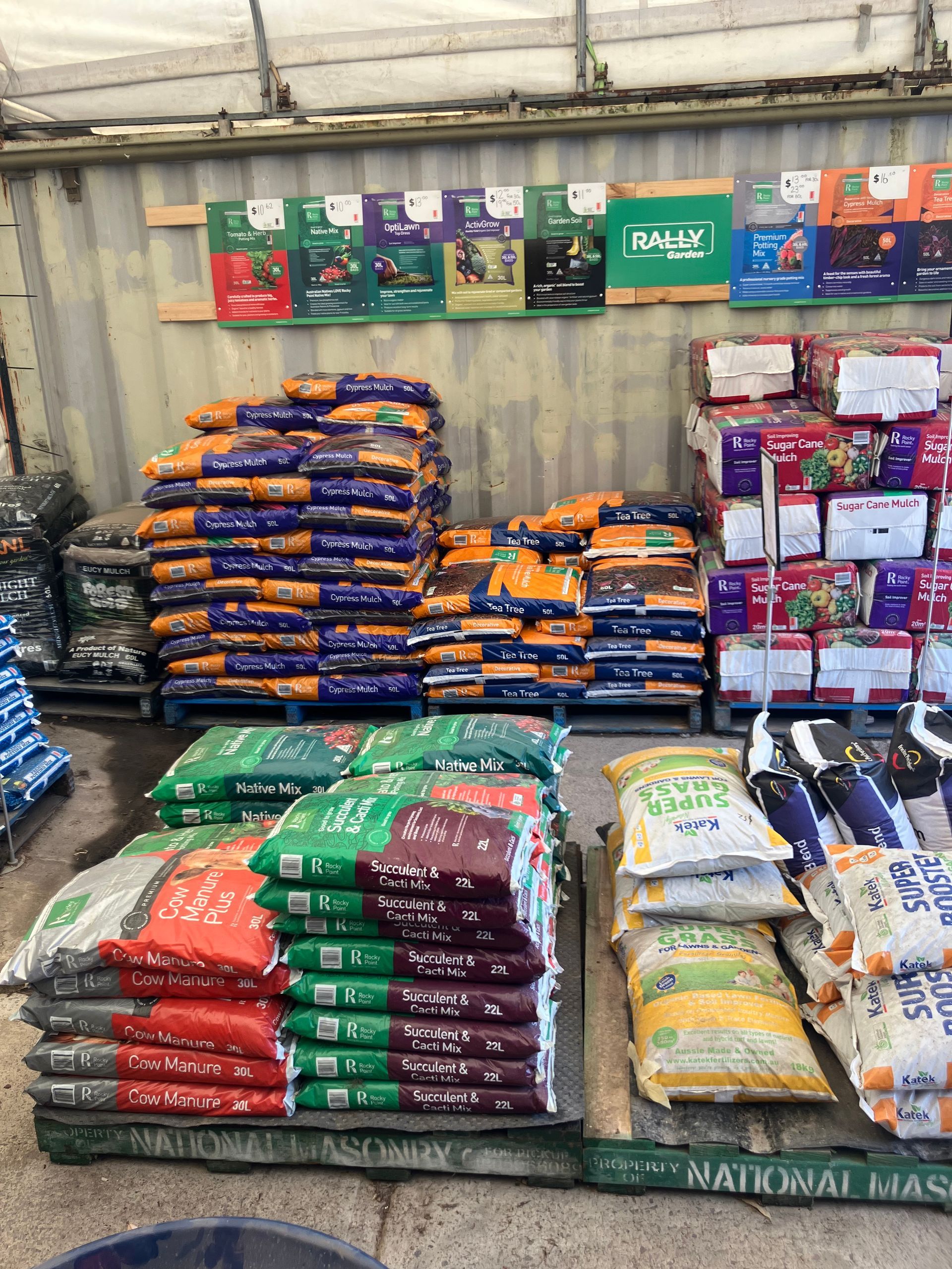 Bags of animal feed stacked on pallets inside a warehouse. Various colors and brands are visible.