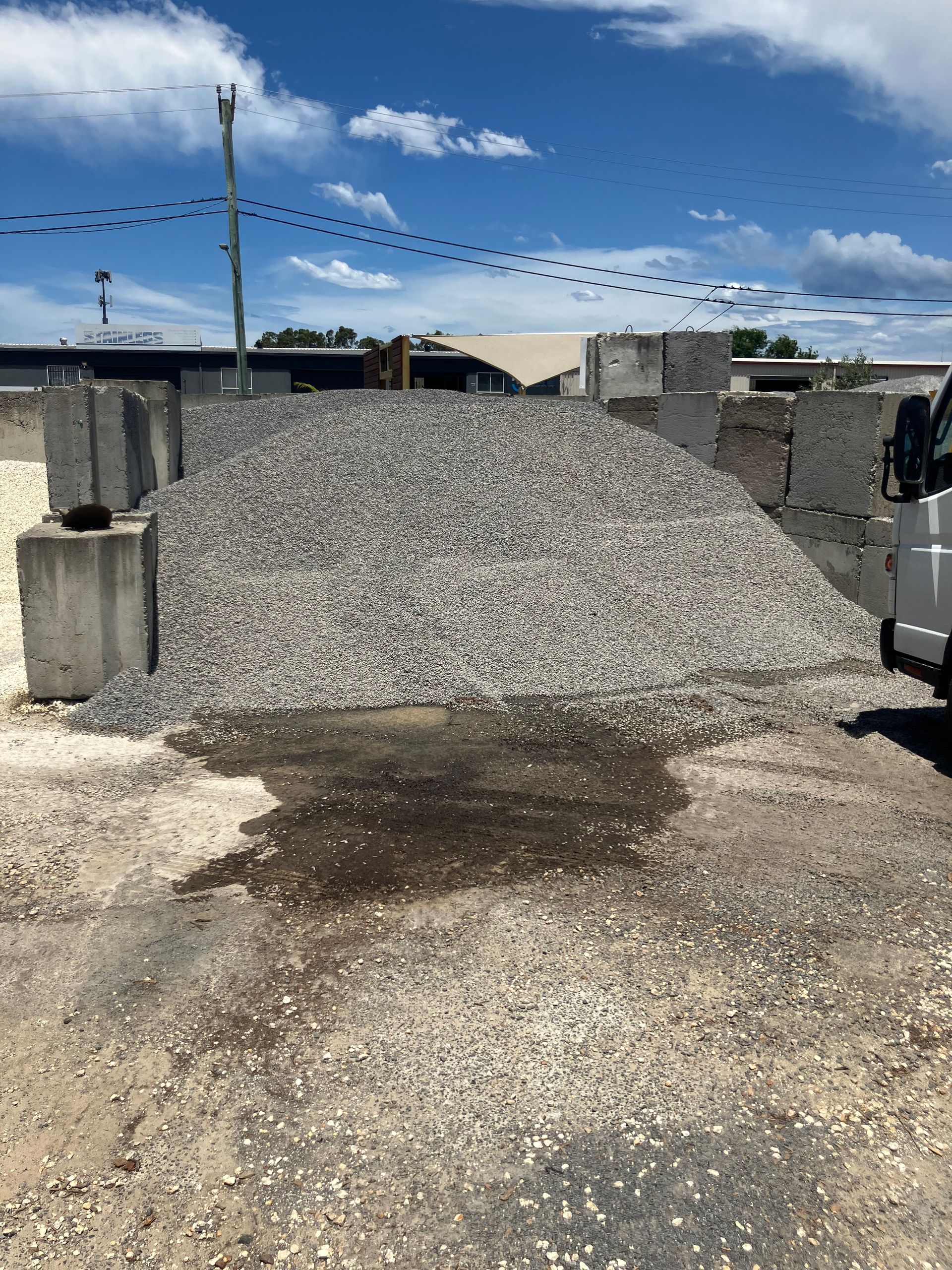 Pile of gravel next to concrete blocks, with a blue sky and parked vehicle.