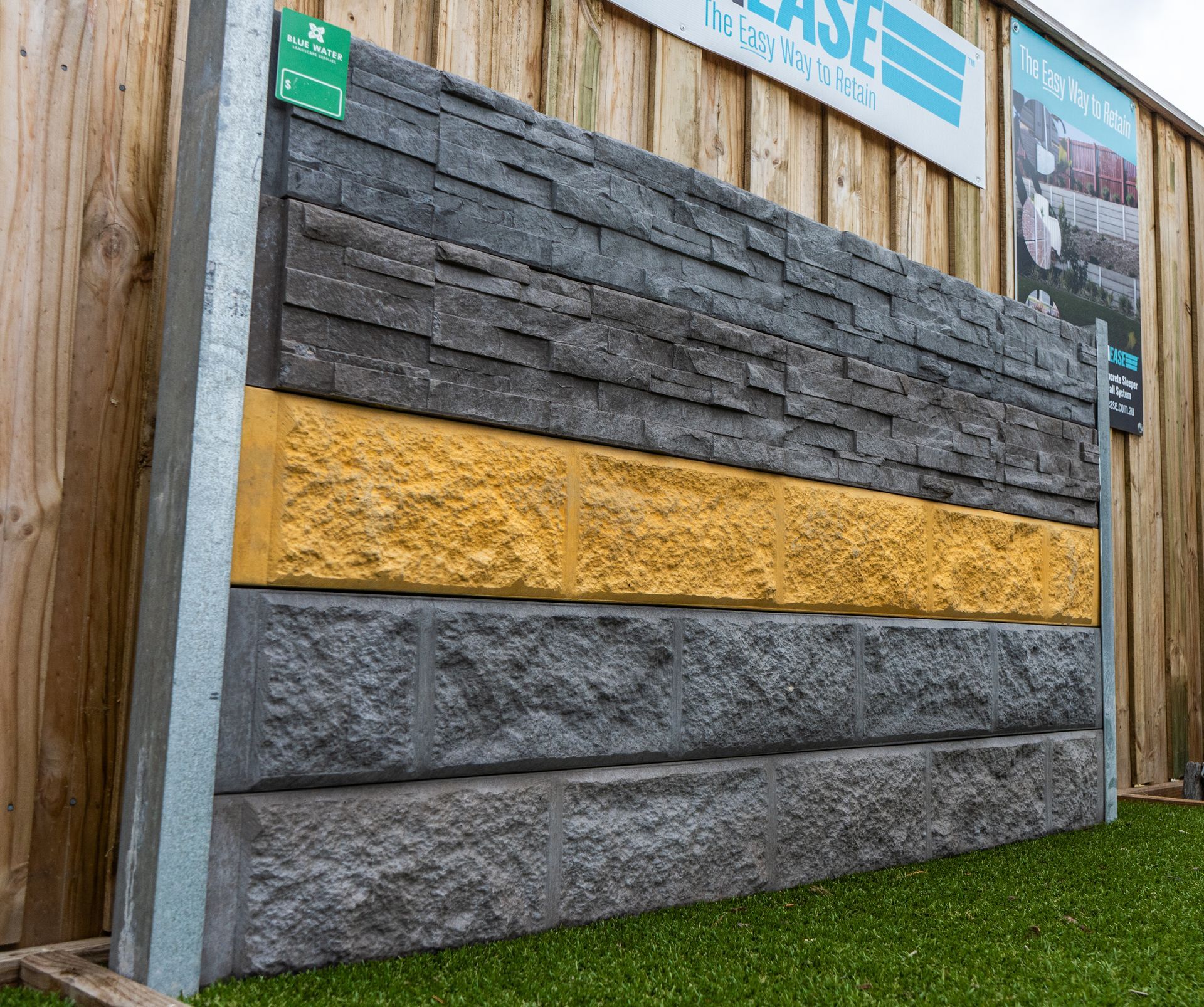Outdoor wall display with stacked gray, black, and yellow textured stone panels on a wooden fence.