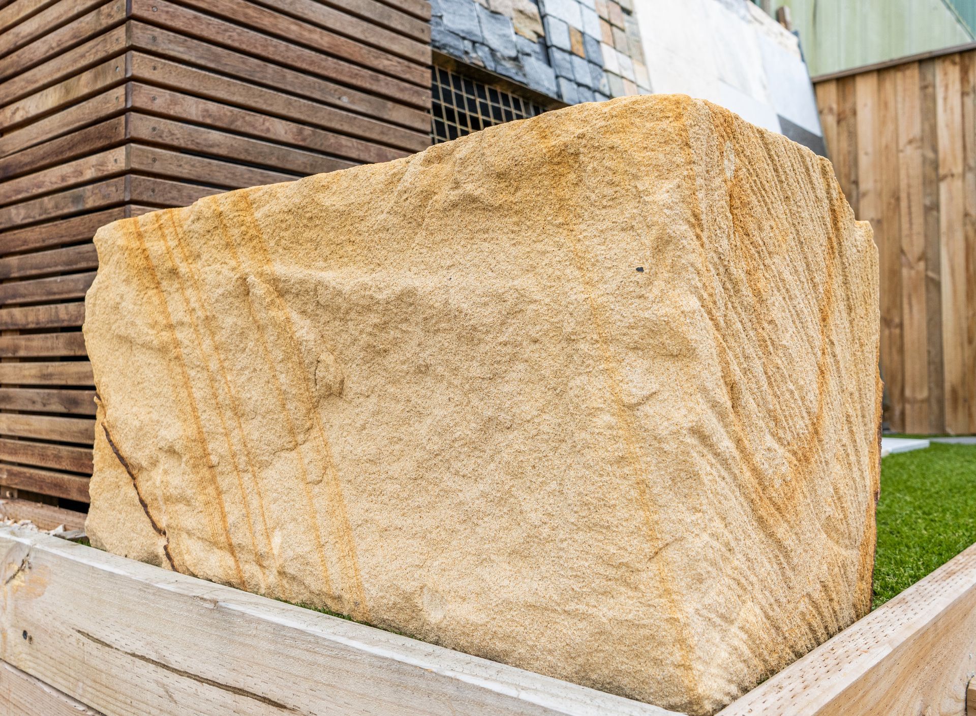 Large beige sandstone block in an outdoor yard beside a wooden fence and brick wall.