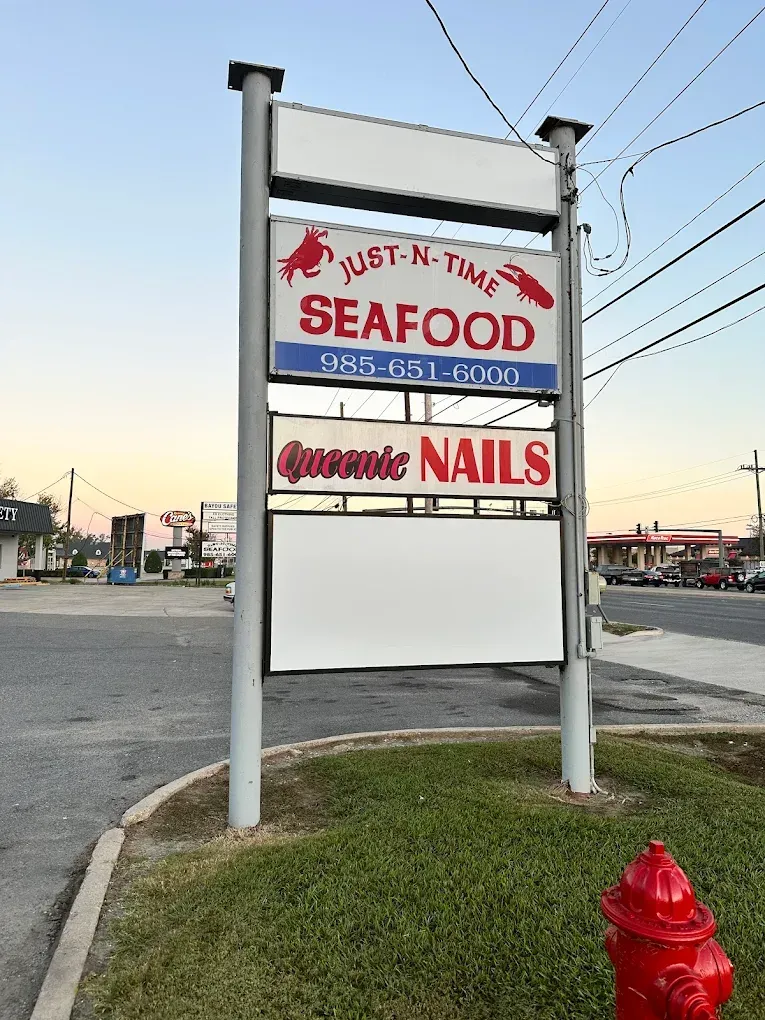 Roadside sign for a seafood market and nail salon beside a red fire hydrant.