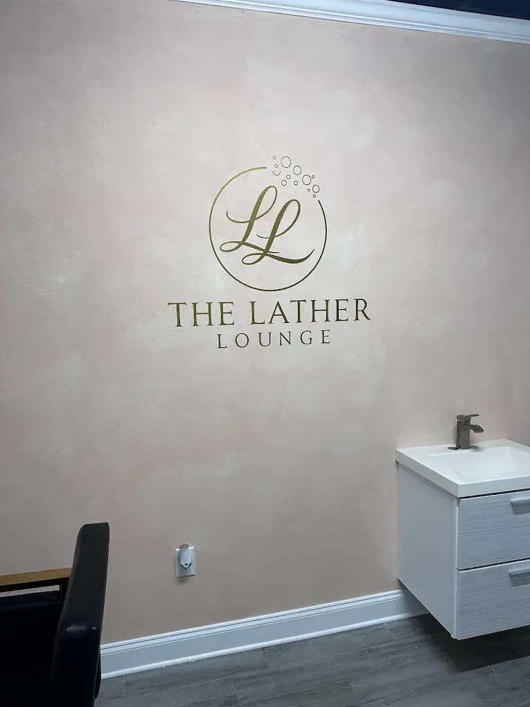 Wall sign with “The Lather Lounge” logo on a beige salon wall, beside a white cabinet.