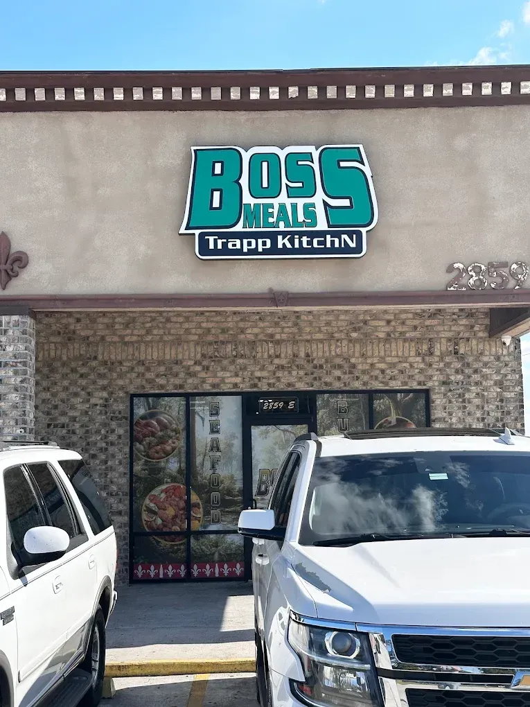 Storefront sign reading “Boss Meals Trapp Kitchen” above parked cars.