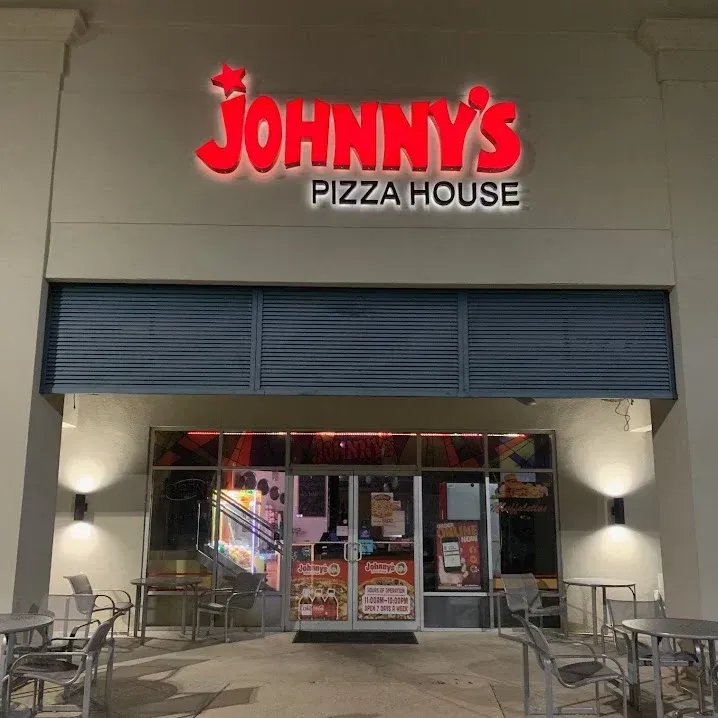 Johnny's Pizza House storefront with red sign and outdoor seating at night