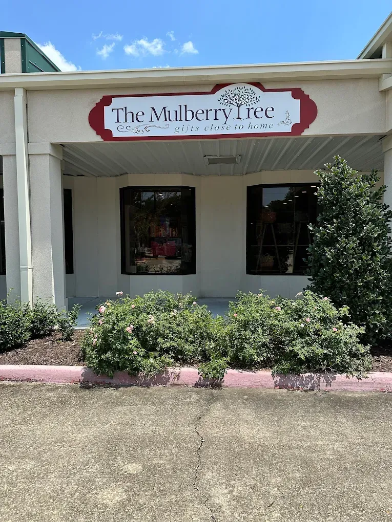 Storefront for “The Mulberry Tree” with white awning, pink flowers, and shrubs in front