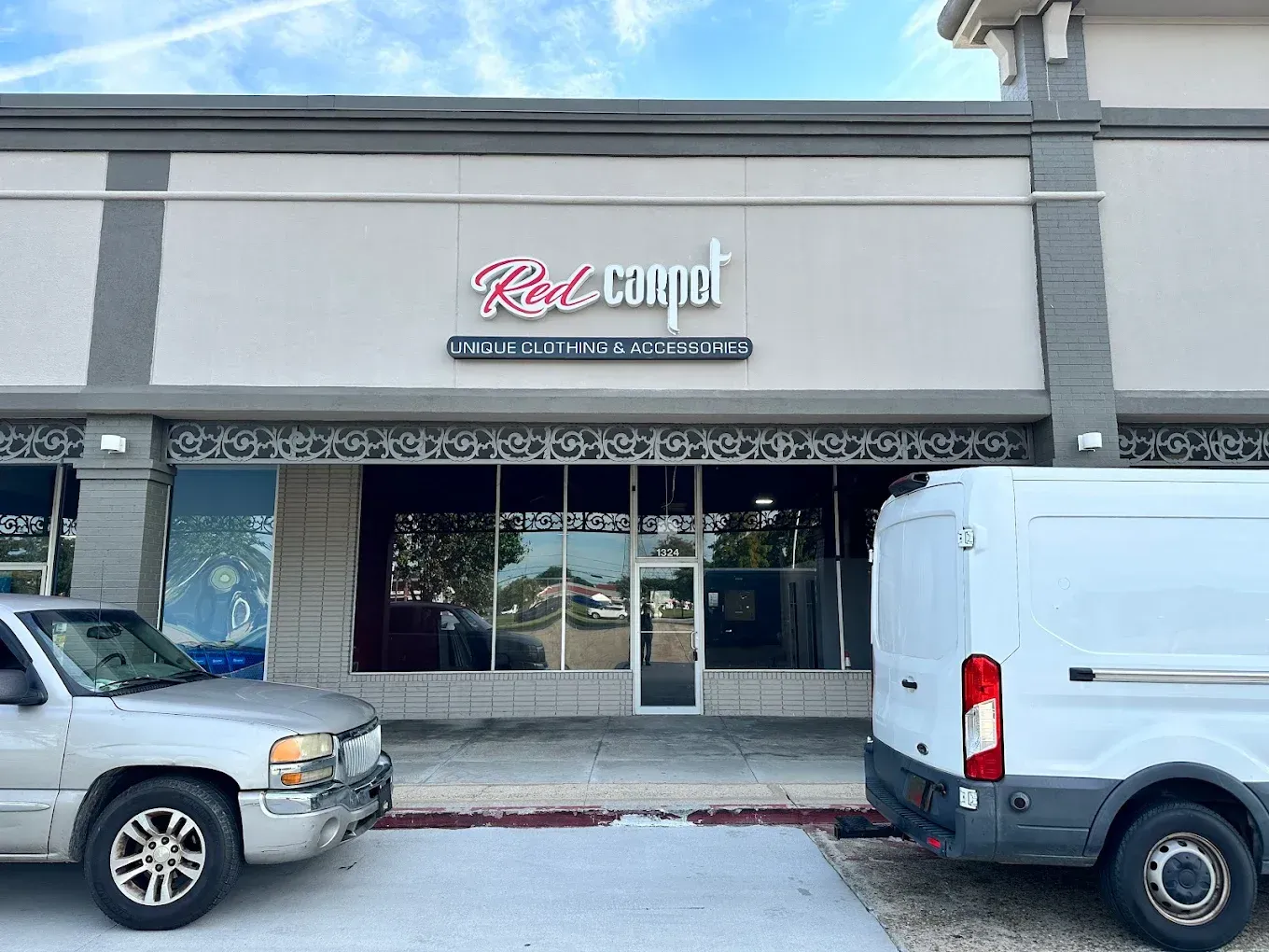 Storefront with a sign above the entrance, parked SUV and white van in front, on a cloudy day