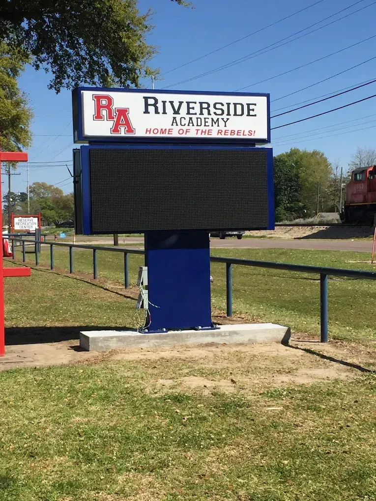 Riverside Academy electronic sign in a grassy field, with school name and logo displayed on top.