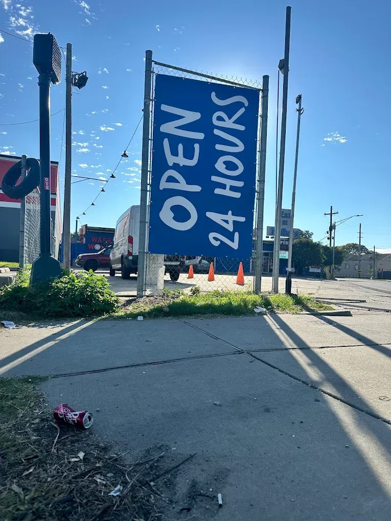 Blue “OPEN 24 HOURS” sign beside a street under a clear sky