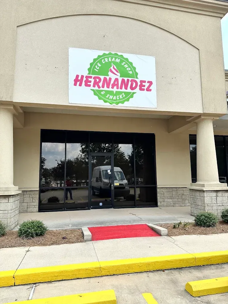 Storefront with a “HERNANDEZ” sign above glass doors and a red curb ramp at the entrance