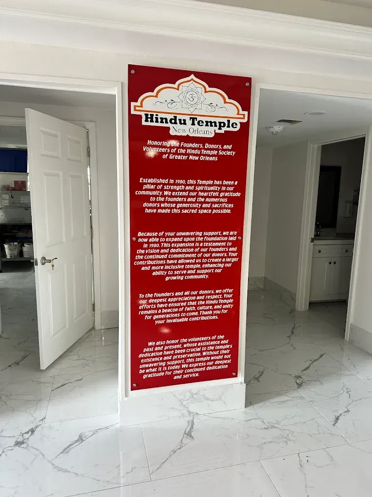 Red informational sign on a white column in a bright marble-floored room with open doors.
