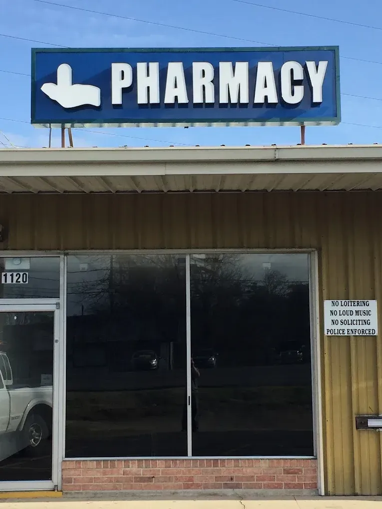 Blue pharmacy storefront sign above a small building with dark windows and a wooden facade