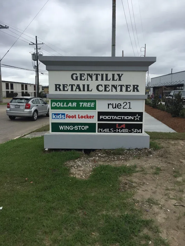 Sign for Gentilly Retail Center with store logos beside a roadside under a cloudy sky
