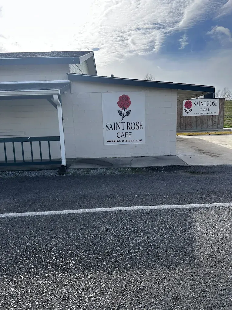 White building with a sign reading “Saint Rose,” seen from a parking lot under a cloudy sky.