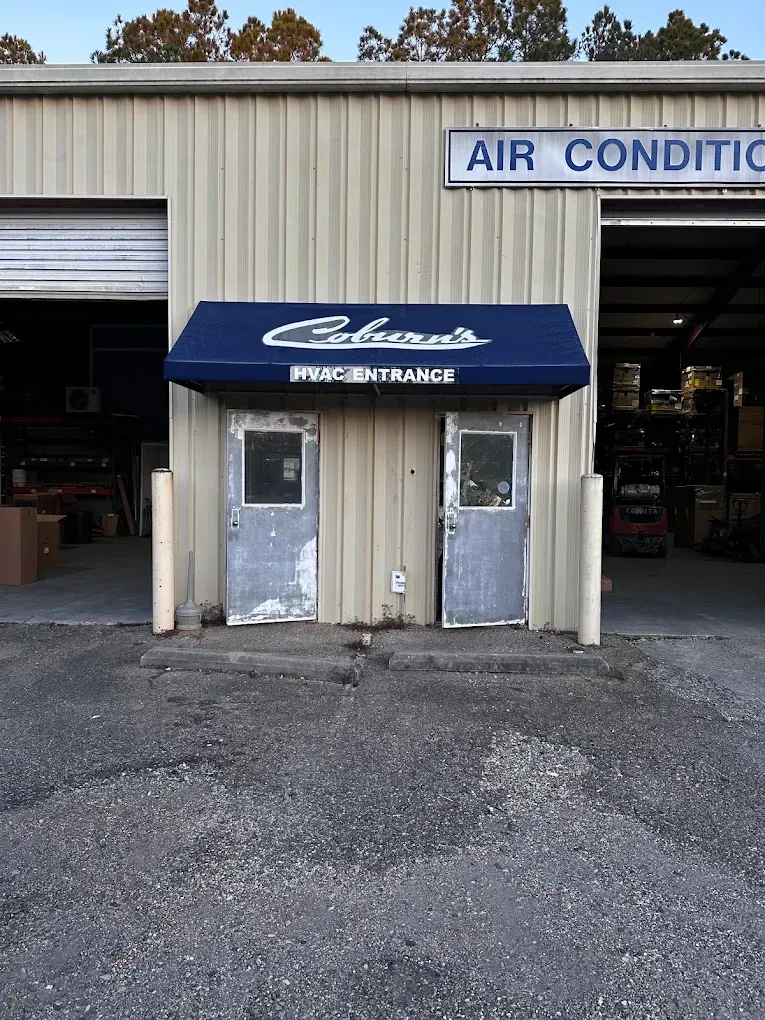 Small blue awning over two white doors at an industrial building entrance, with an “AIR CONDITI…” sign above.