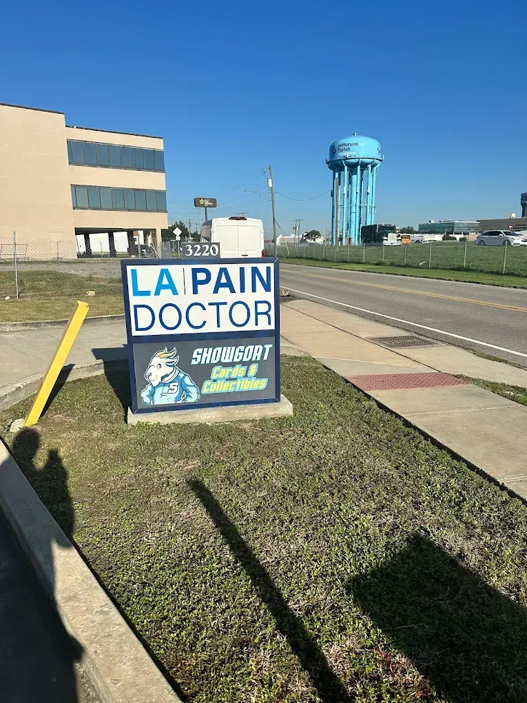 Sign for “La Pain Doctor” on a roadside lawn beside a building, with a water tower in the background.