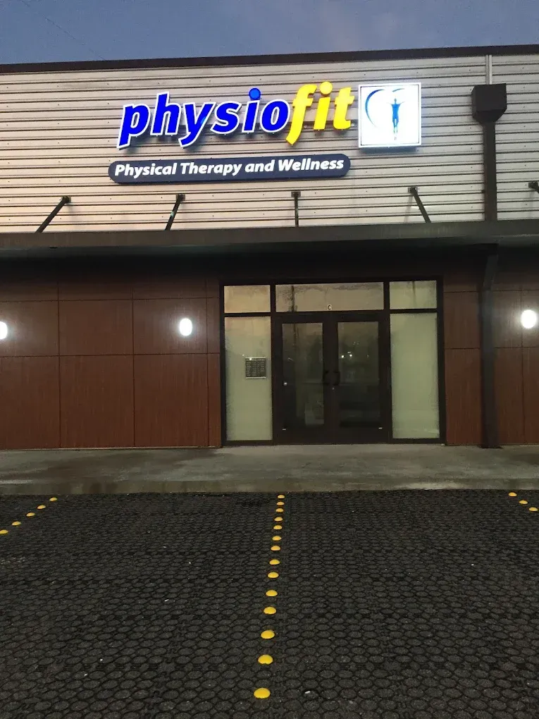 Physiofit physical therapy storefront at night with lit sign and glass entrance.