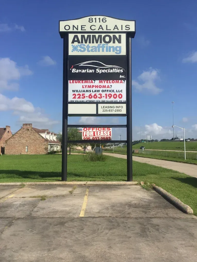Tall roadside sign for Ammon Staffing on a concrete base beside a grassy field under a blue sky.