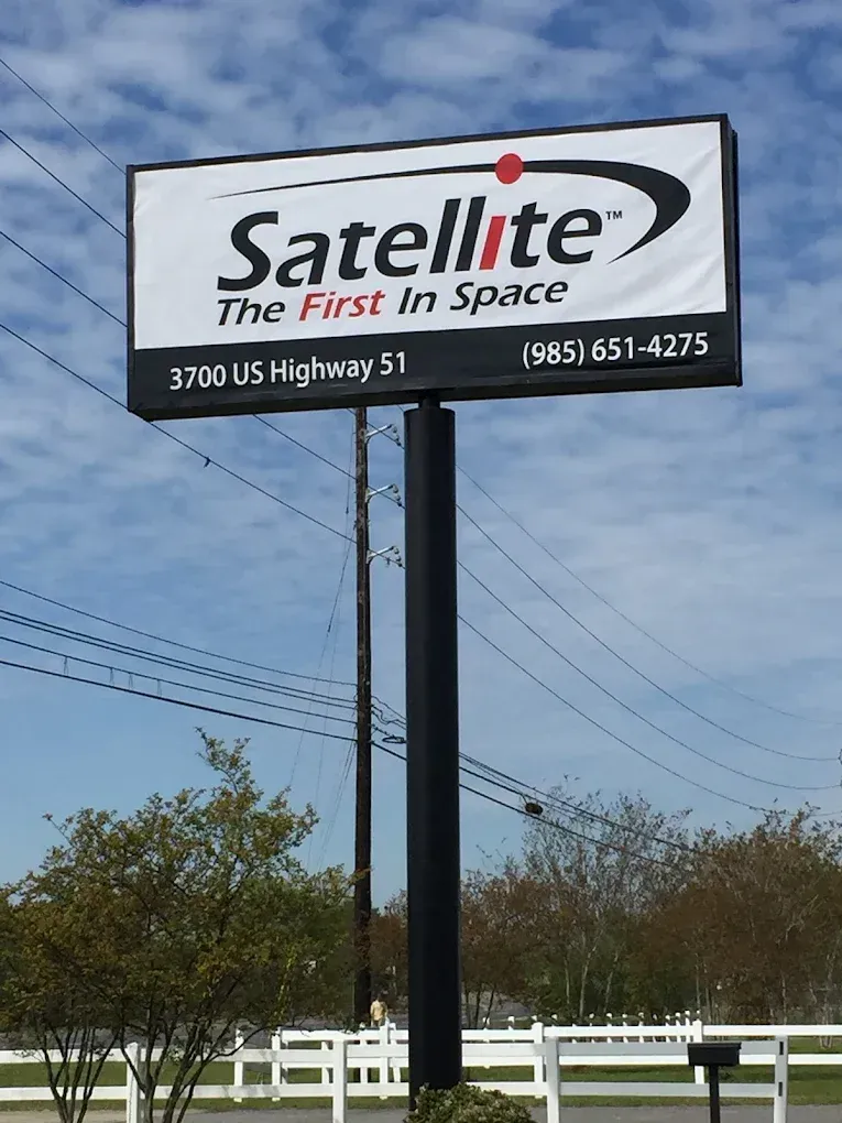 Satellite store sign beside a road, reading “The First in Space” with phone number and address.