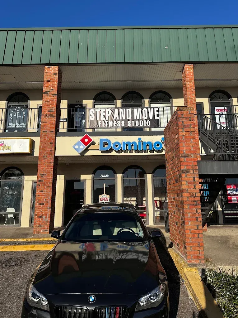 Storefront with Domino's and other businesses under a covered brick arcade, with a black car parked in front.
