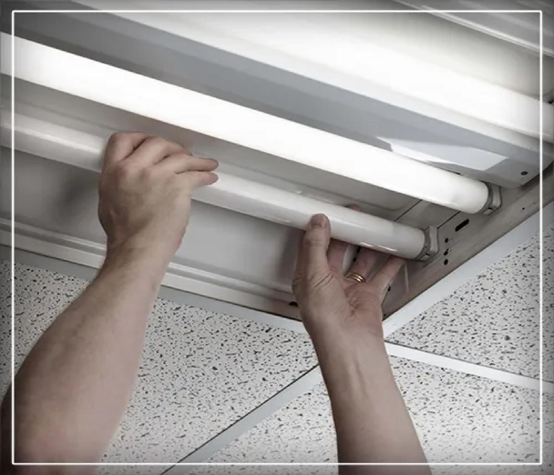 Hands replacing a fluorescent ceiling light tube in a drop ceiling fixture
