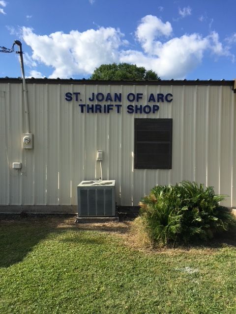 St. Joan of Arc Thrift Shop sign on a white building under a blue sky.