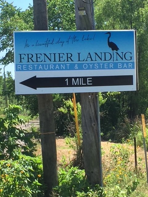 Blue roadside sign for Frenier Landing Restaurant & Oyster Bar with left arrow, “1 mile” text.