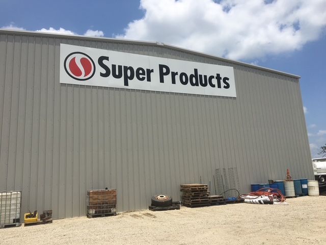 Super Products warehouse exterior with sign, pallets, and equipment along the wall