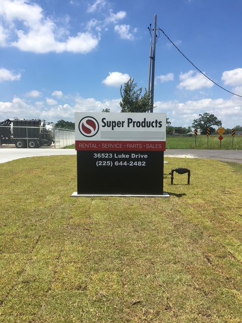 Super Products sign on a grassy roadside under a blue sky with clouds