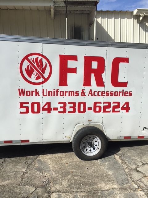 White FRC work-uniforms trailer with red logo and phone number parked by a building