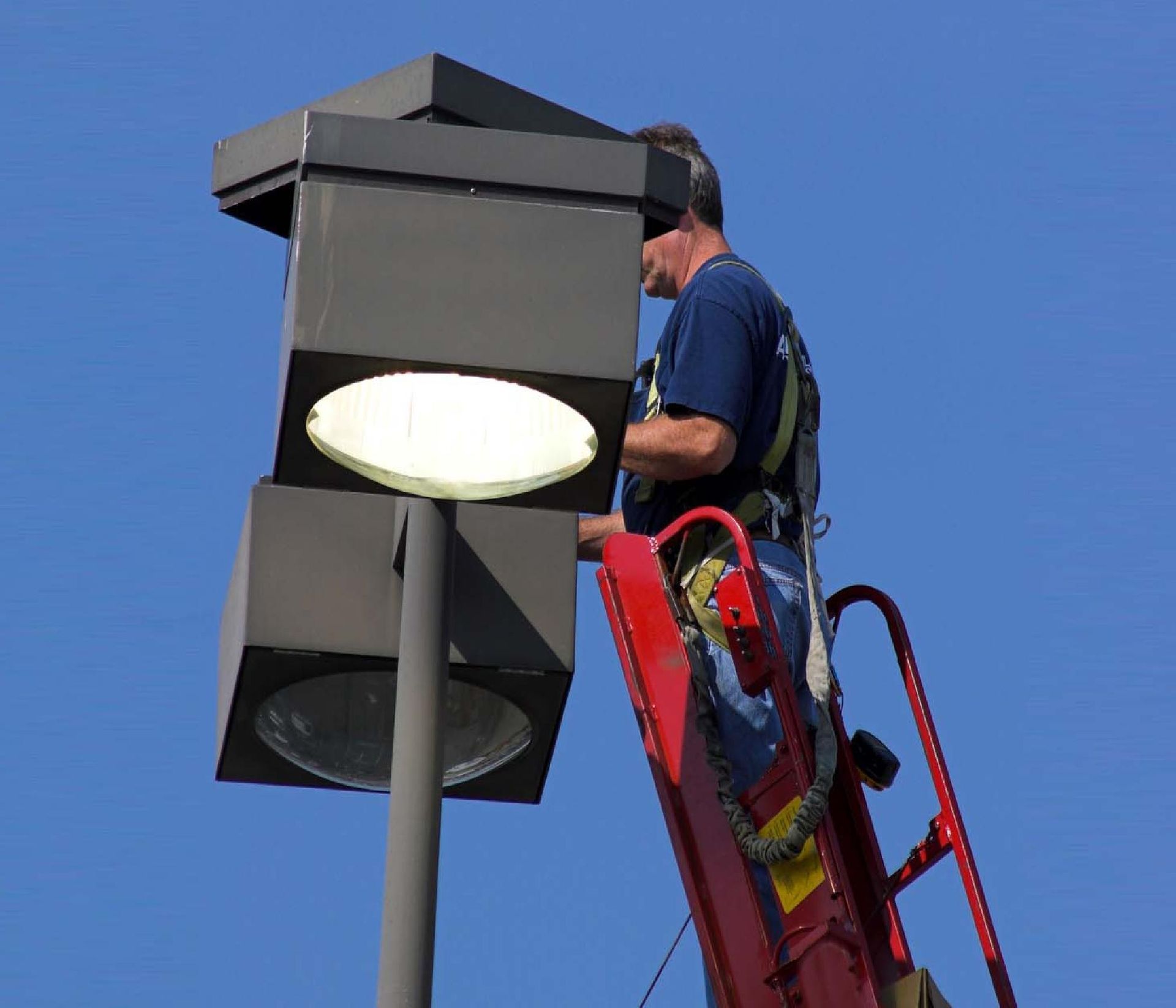 Worker on a red ladder servicing a streetlight against a blue sky