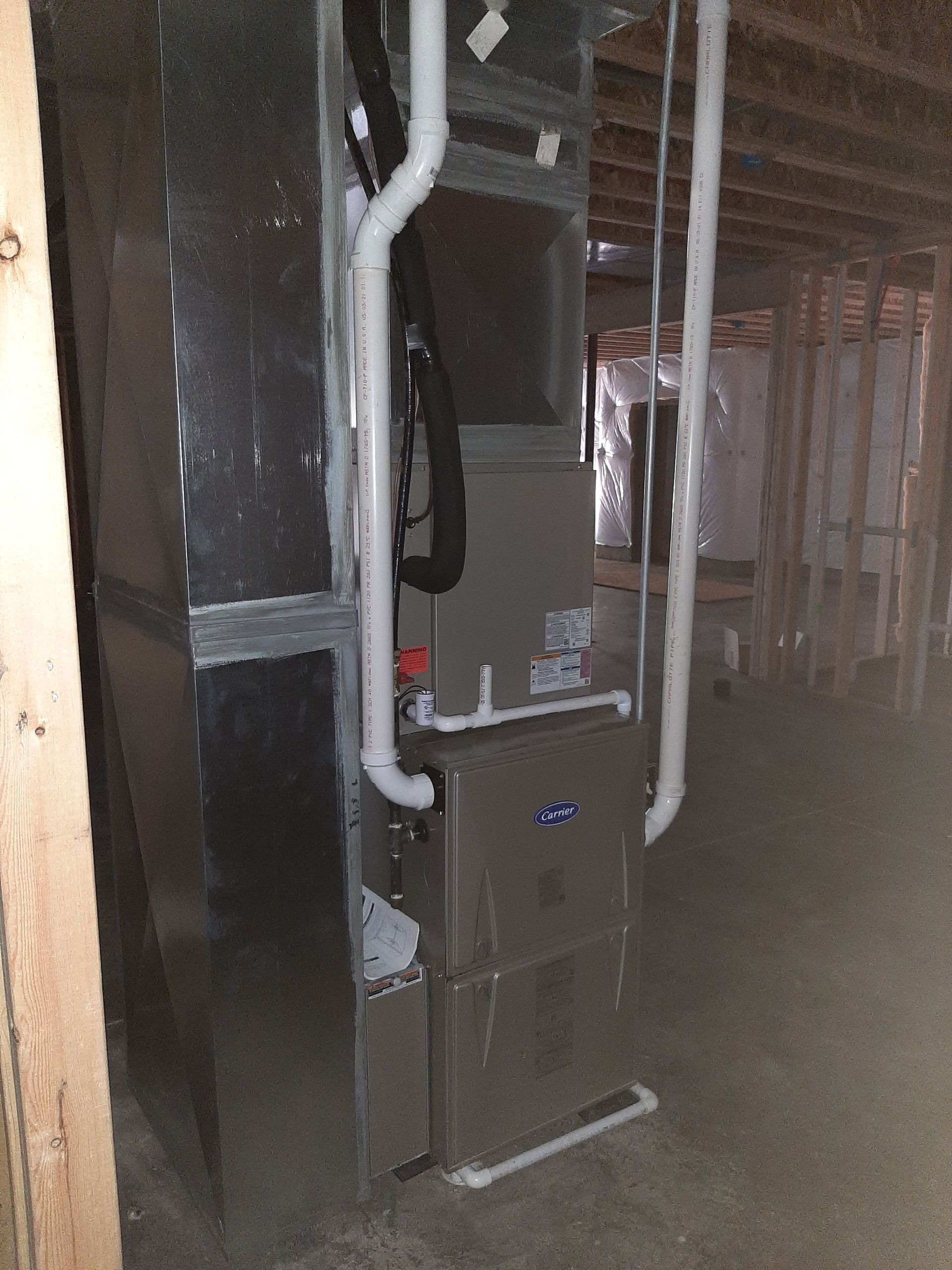 HVAC system in a basement setting with ductwork and PVC pipes. Gray metal unit with a silver casing.