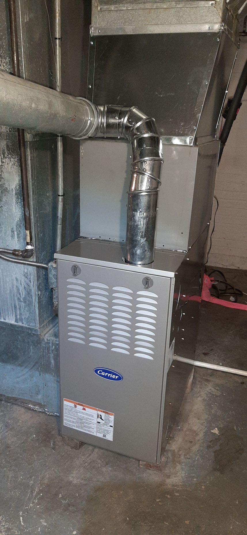 Furnace installed in a basement, with exhaust pipe. Gray metal and concrete.