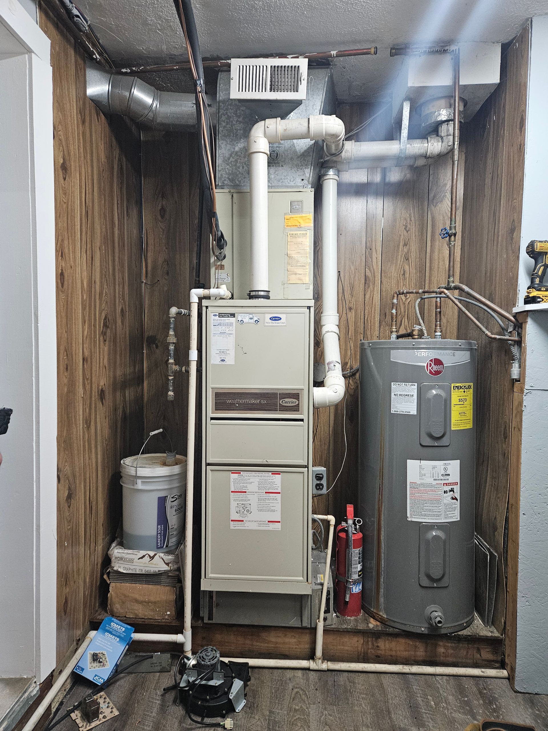 A furnace and water heater are installed in a utility closet with wood paneling.