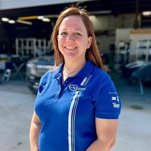 Woman in blue polo smiling, standing in front of a garage.