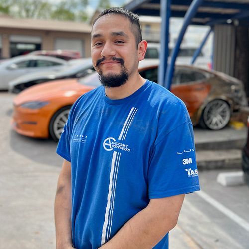 Man in blue shirt, smiling in front of cars, likely at a shop.
