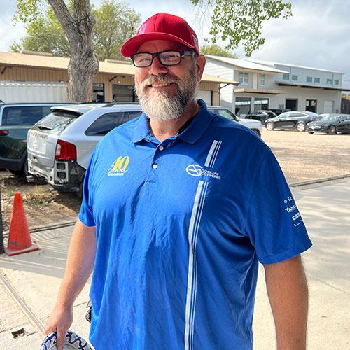 Man in blue shirt and red cap, smiling outdoors, holding plate, cars in background.