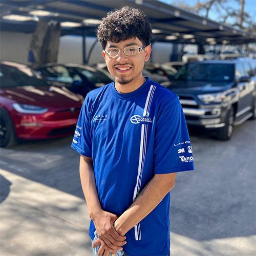 Man in blue Subaru shirt, smiling, in front of cars, outdoors.