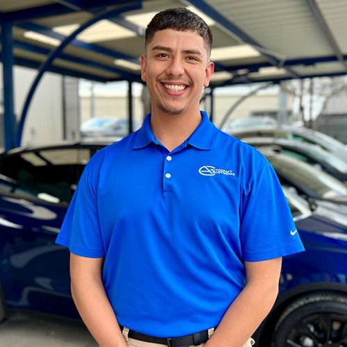 Man in blue polo smiles, standing near cars in a carwash setting.