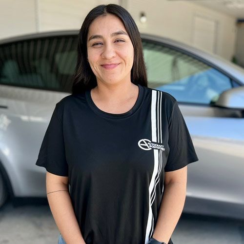 Woman in black shirt smiling in front of a silver car.