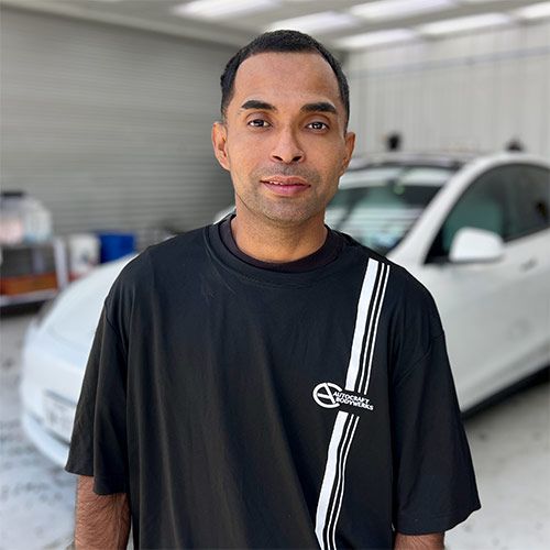 Man in a black polo shirt, standing indoors with a Tesla sign in the background.