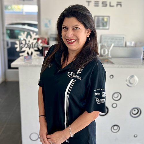 Woman in a black shirt, smiling, in front of a counter with a TESLA sign in the background.