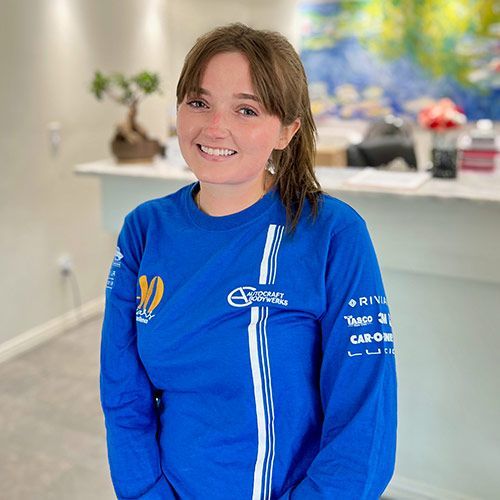 Woman with brown hair in blue long-sleeve shirt with logos smiles in a room.